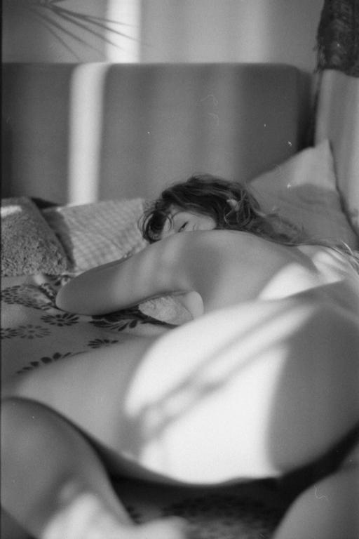 A woman lies on a bed with light and shadow patterns across her body.