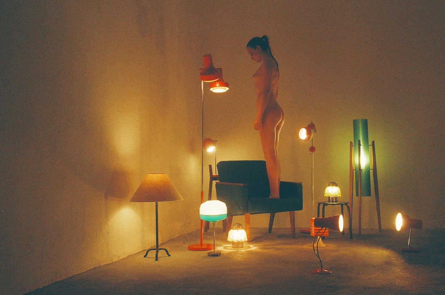 A woman stands on a chair surrounded by various lamps in a room.