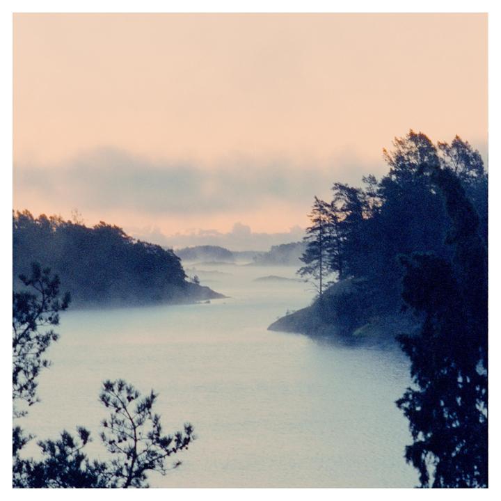 A body of water is surrounded by islands and trees under a hazy sky.