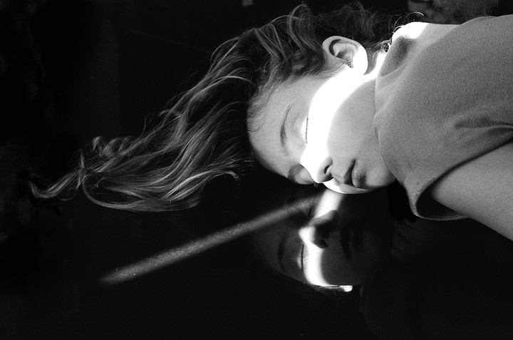 A girl with long hair sleeps with a beam of light across her face, reflected on a dark surface.