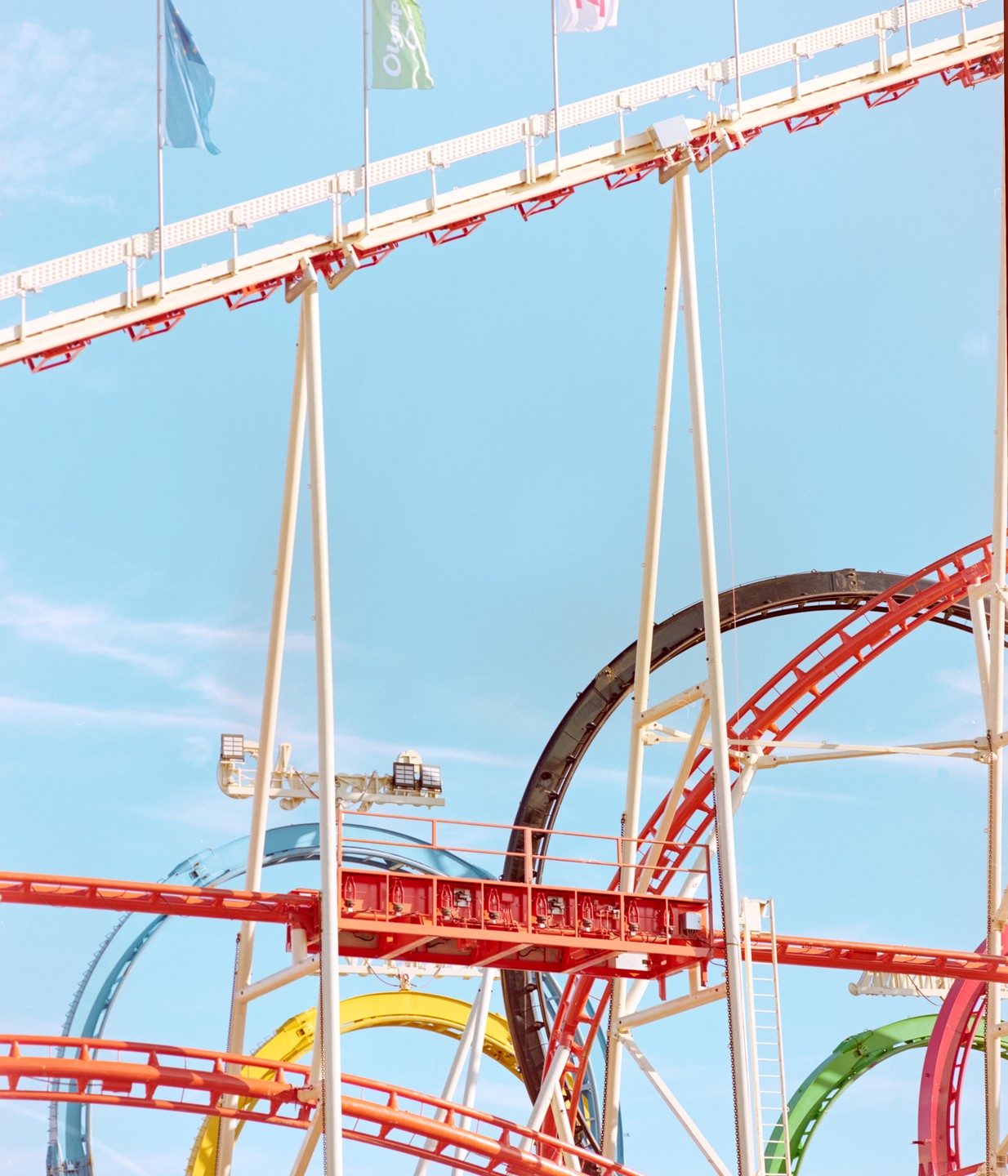 A colorful rollercoaster with multiple tracks twists against a clear blue sky with flags.