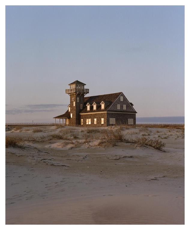 A large wooden building with a tower stands on a sandy beach at dusk.