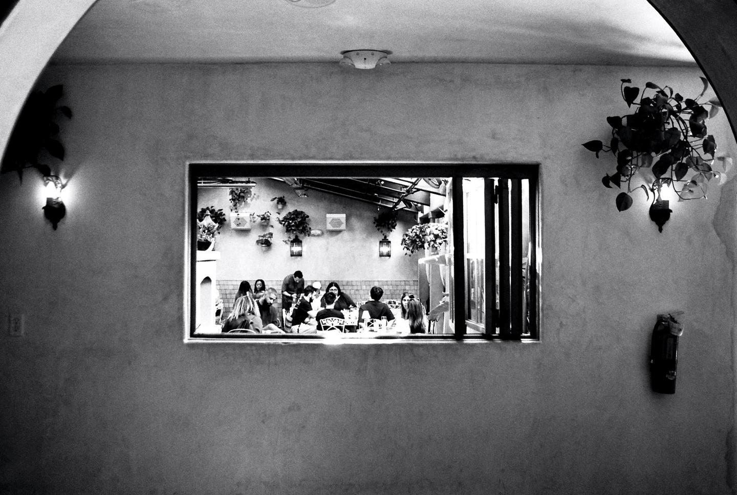 A group of people are visible through a window, sitting at tables in a restaurant.
