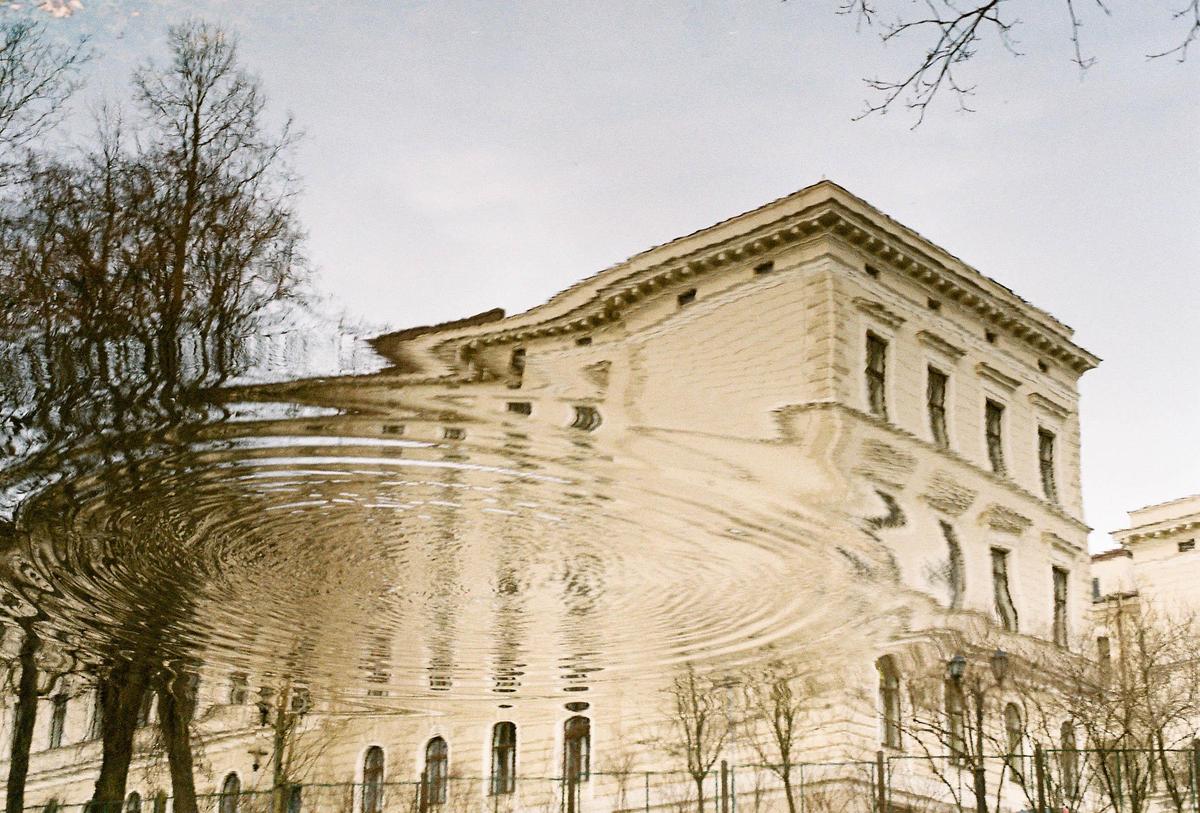 A building and trees are reflected in rippling water.