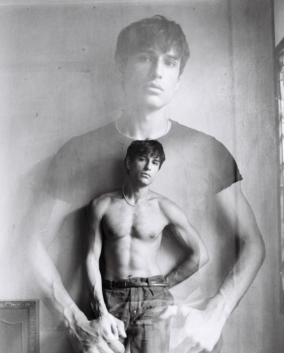 A man with a pearl necklace is captured in a double exposure, with one exposure showing him shirtless and the other showing him wearing a t-shirt.