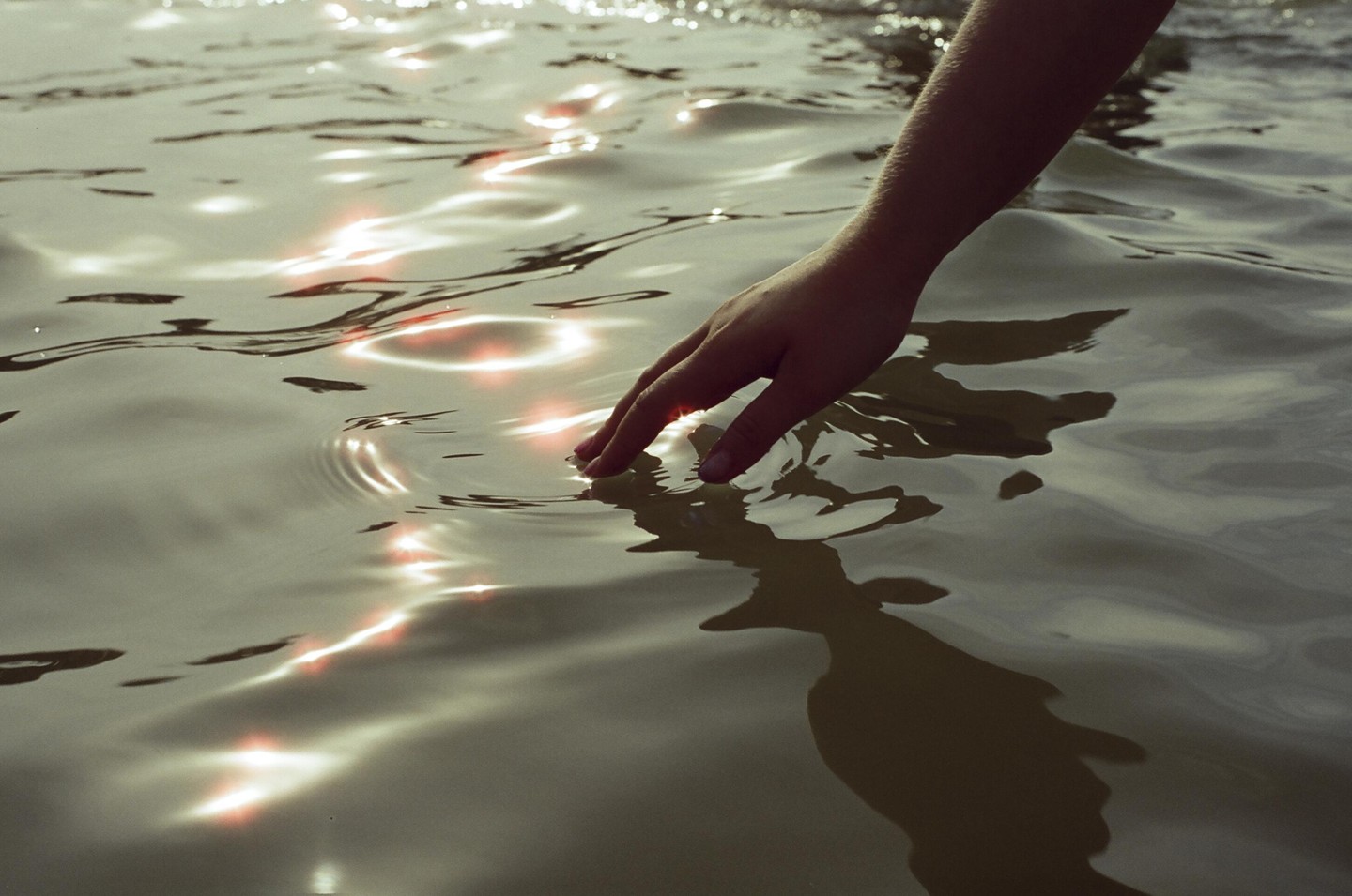 A hand reaches into shimmering water, creating ripples.