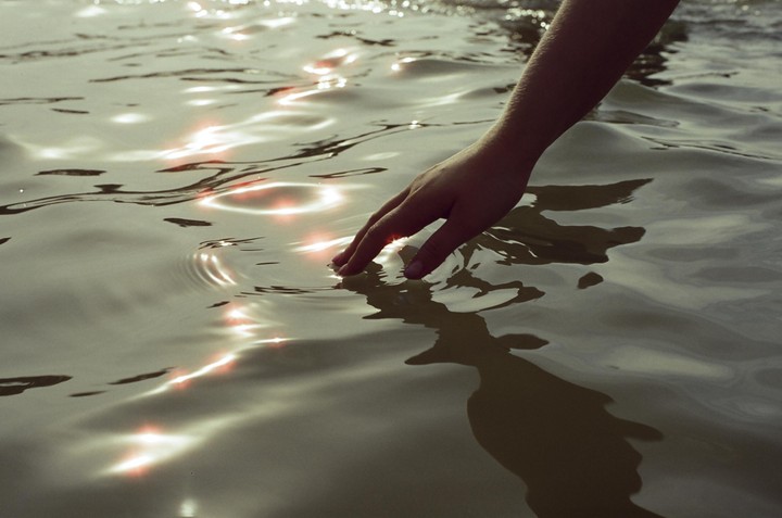A hand reaches into shimmering water, creating ripples.