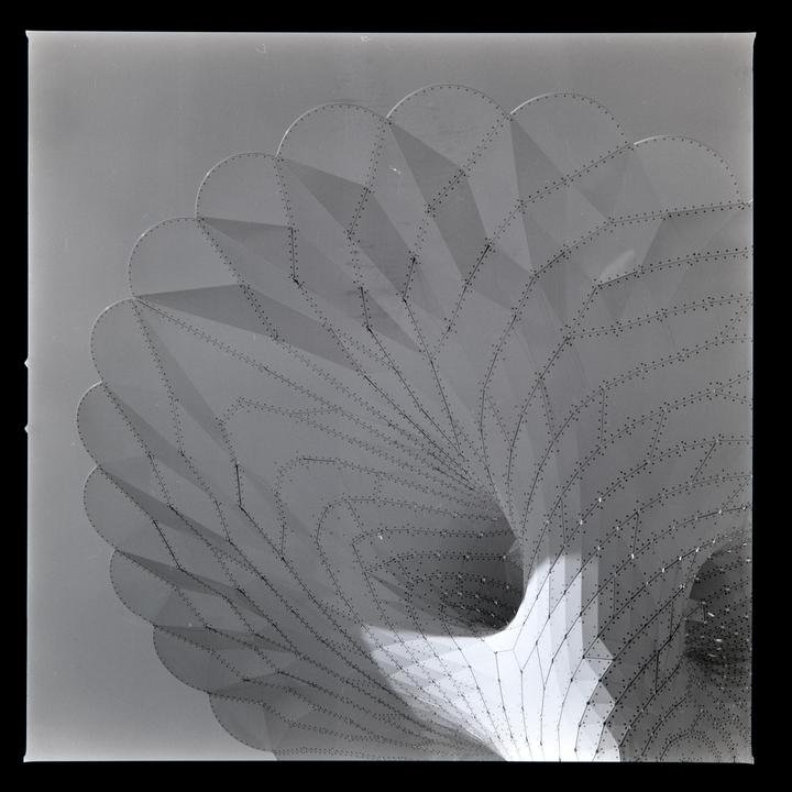 A large, curved, perforated metal structure with a scalloped edge is shown from below.