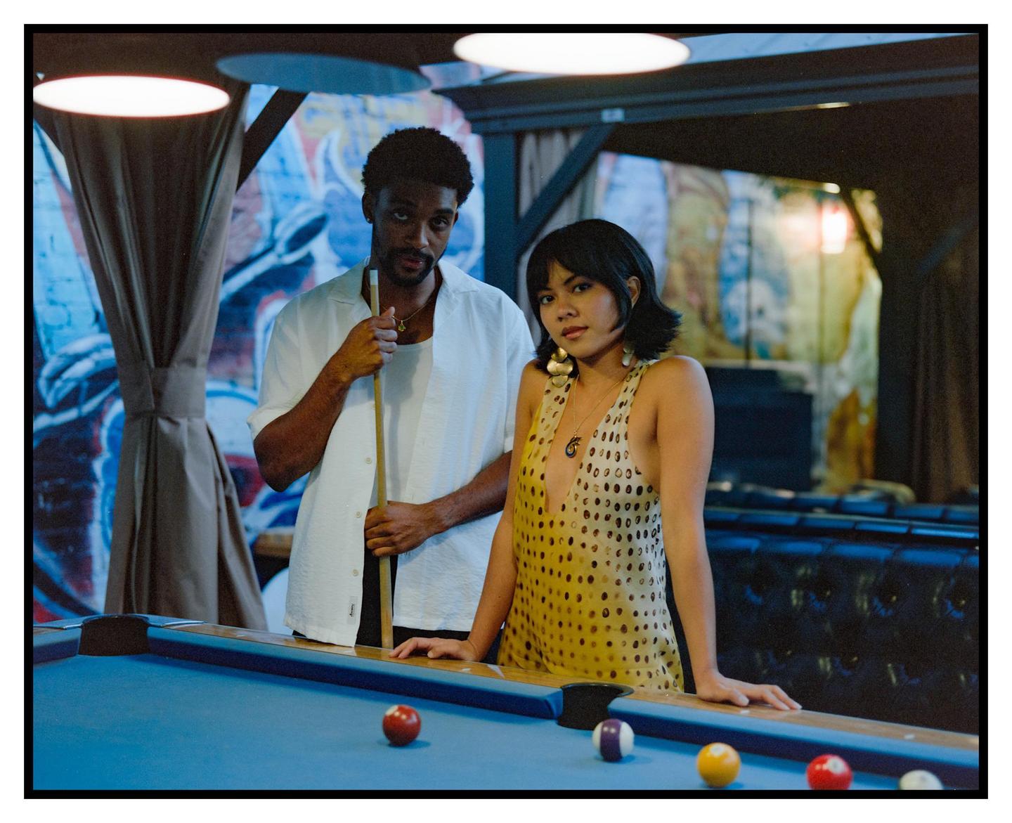 A man and a woman stand next to a pool table with billiard balls on it.