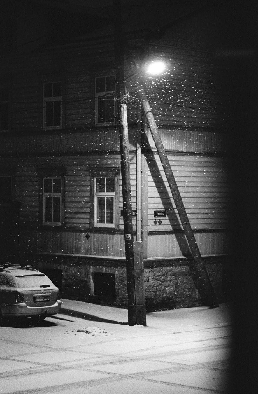 A street light illuminates falling snow next to a building and a parked car.