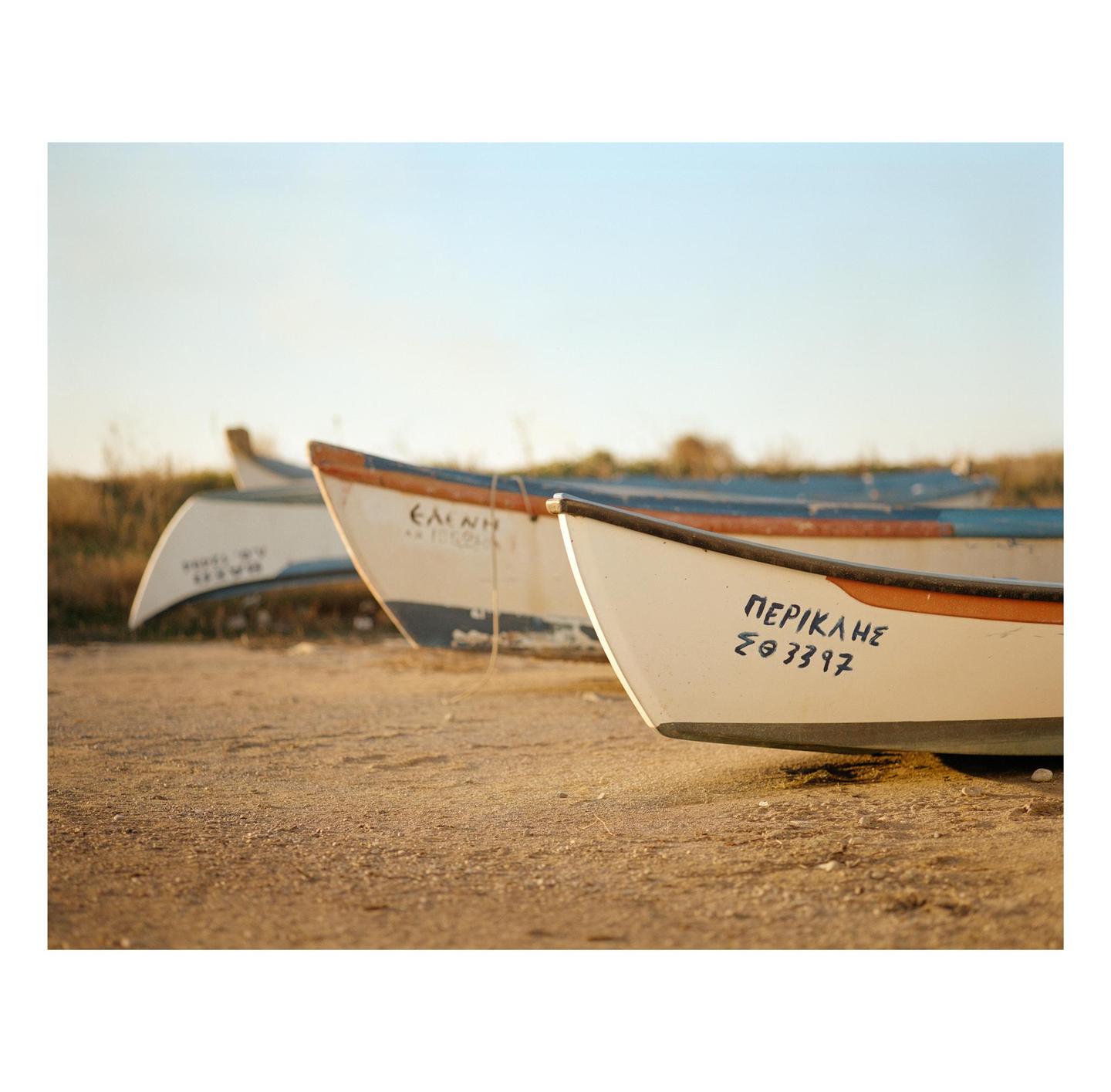 Three small boats are lined up on a sandy beach under a clear sky.