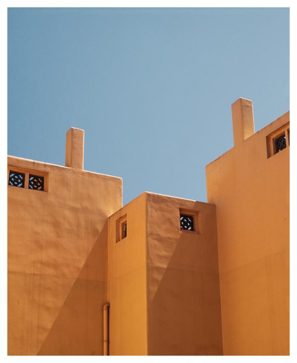 A building with orange walls and small windows is shown against a clear blue sky.