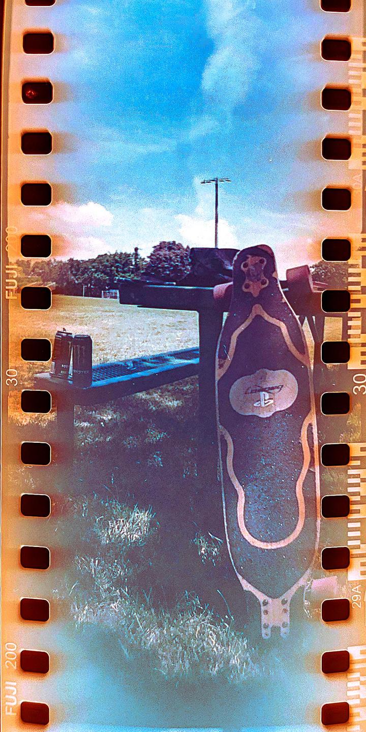 A longboard leans against a picnic table in a grassy field under a bright blue sky.