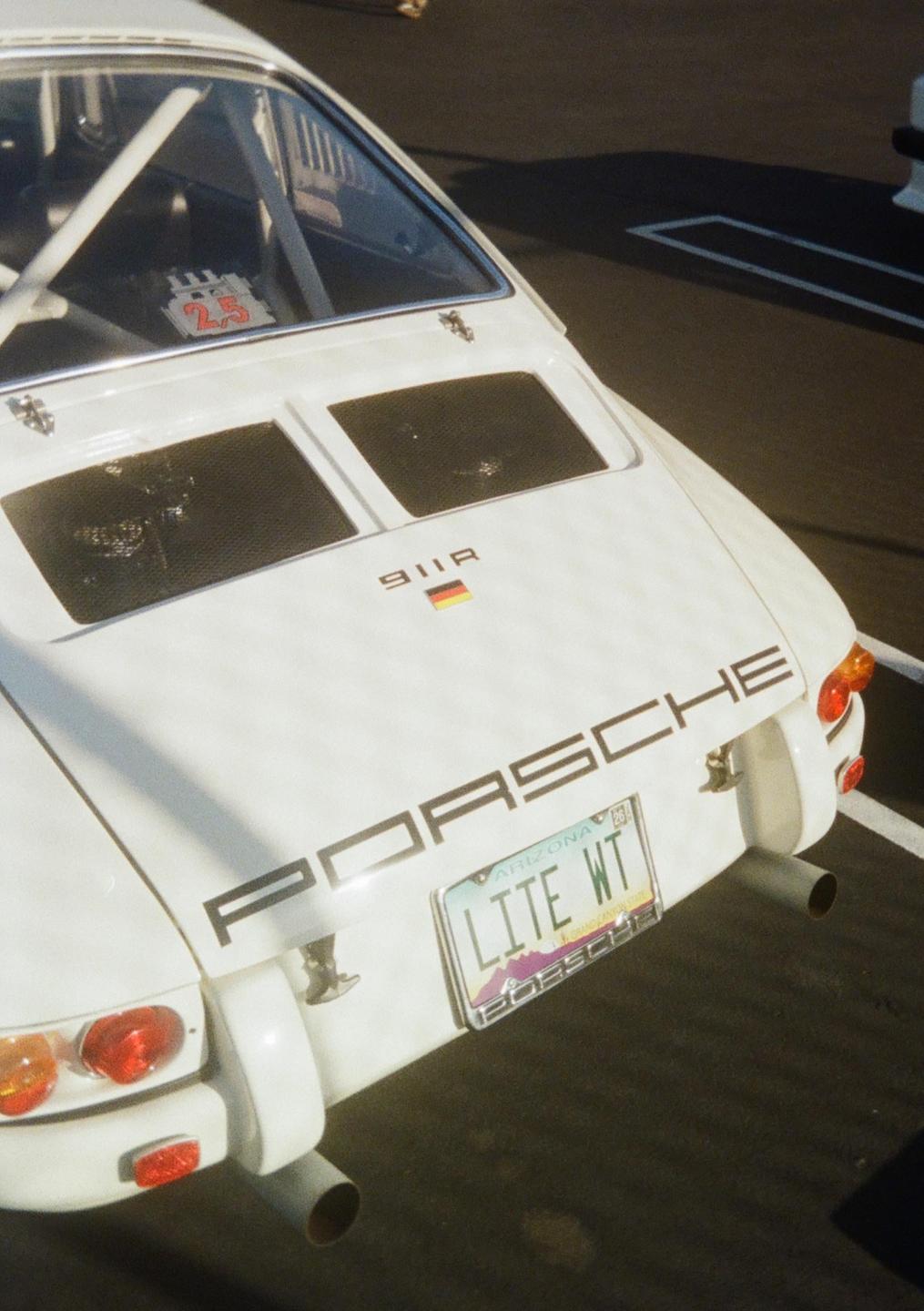 The rear of a white Porsche 911R with an Arizona license plate is parked on asphalt.