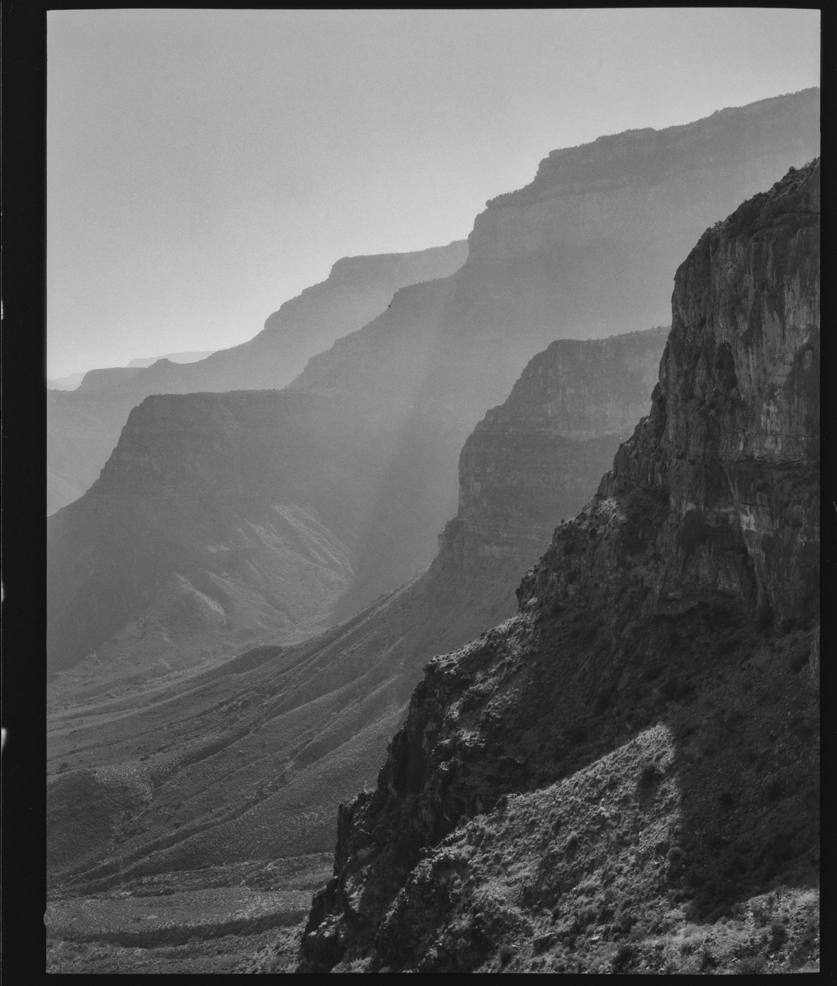 A hazy view of the Grand Canyon shows multiple layers of mountains and a valley.