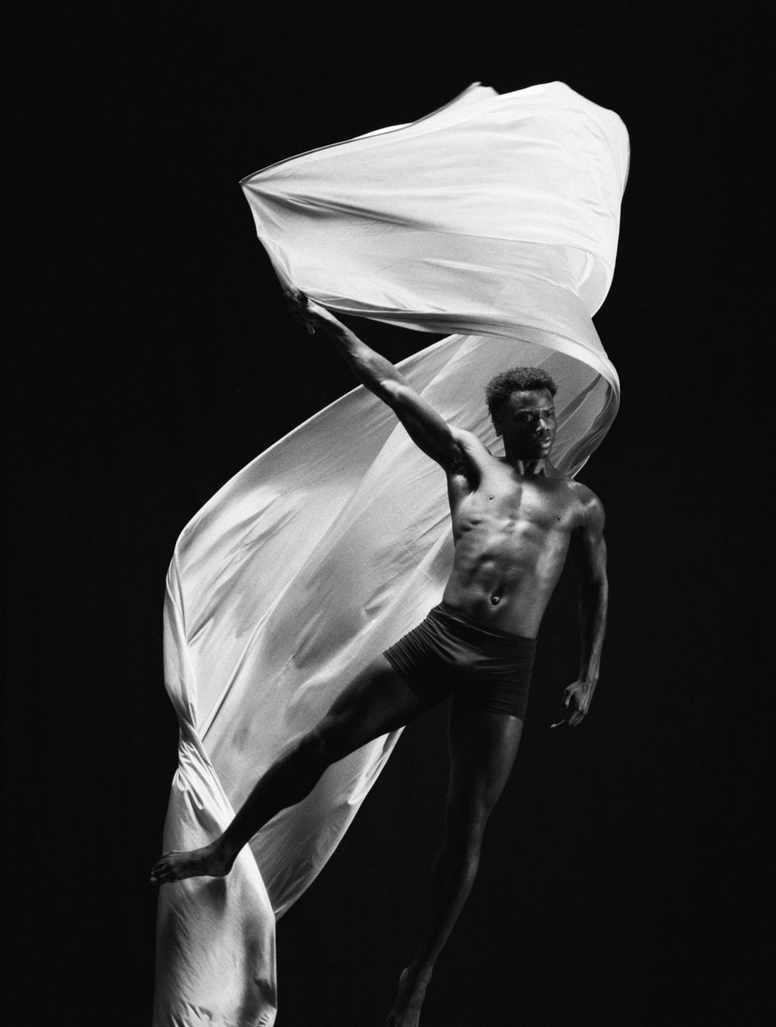 A man in motion holds a flowing piece of fabric against a dark background.