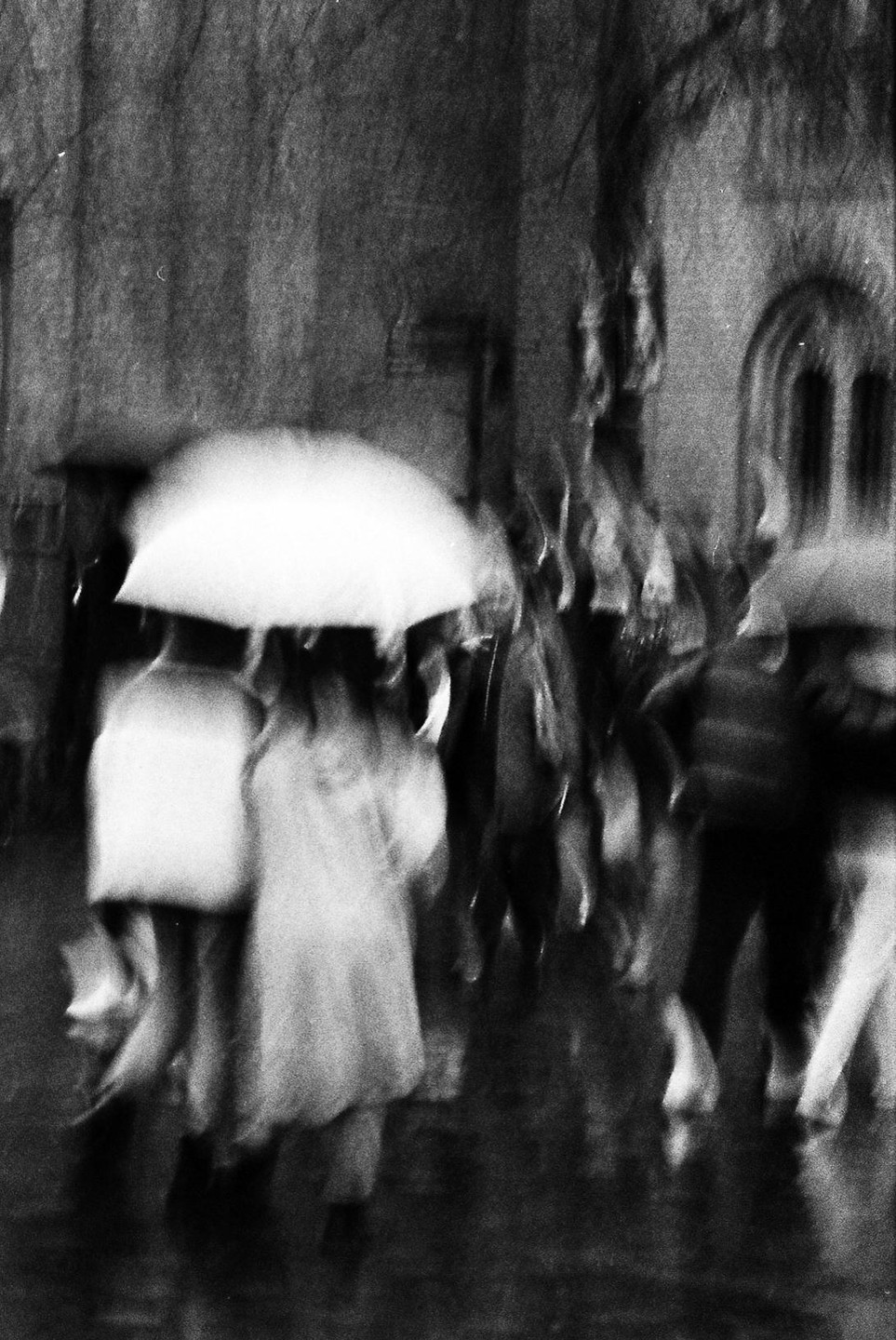 A blurry street scene shows people walking with umbrellas in the rain.