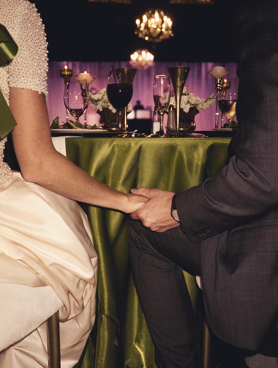 A couple holds hands under a table set with drinks and candles.
