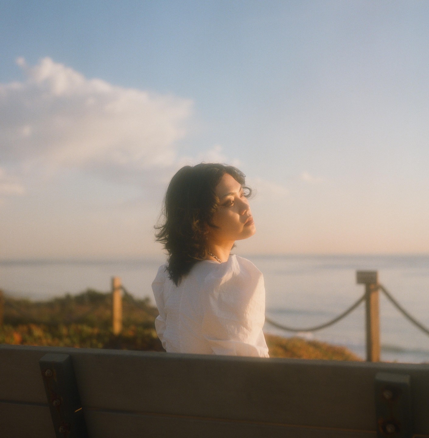 A woman sits on a bench overlooking the ocean at sunset.