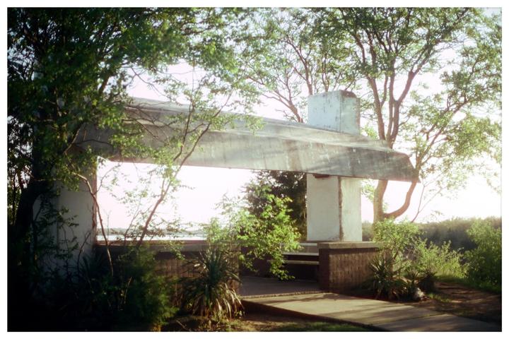 A concrete structure with a flat roof is surrounded by lush green trees and bushes.