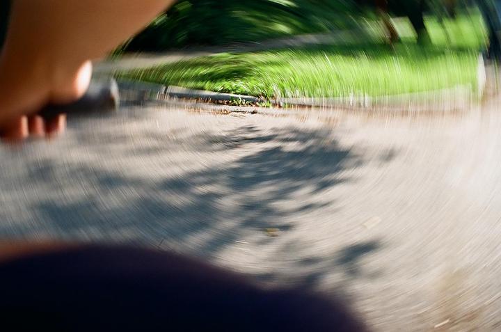 A hand is visible in the foreground of a blurry image of a path next to grass.