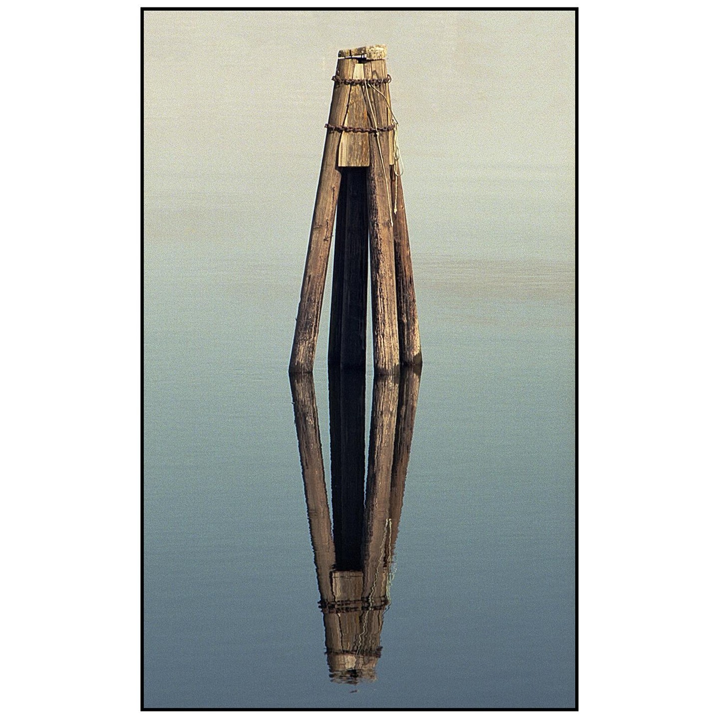Three wooden posts stand in calm water, reflecting in the surface.
