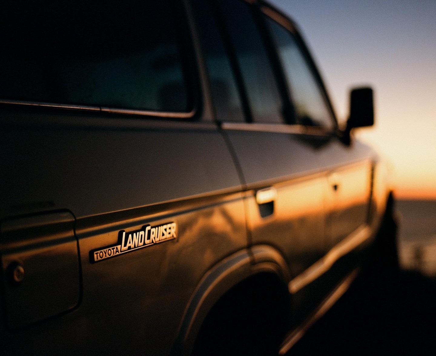 The side of a Toyota Land Cruiser is illuminated by the golden light of sunset.