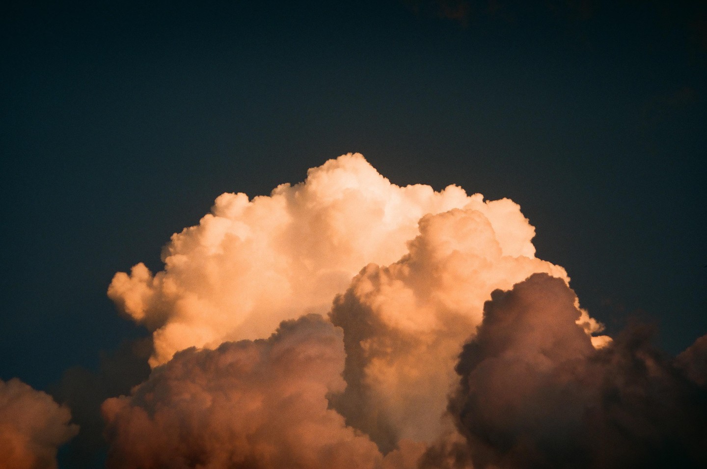 A large, fluffy cloud is illuminated by the setting sun against a dark sky.
