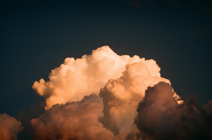 A large, fluffy cloud is illuminated by the setting sun against a dark sky.