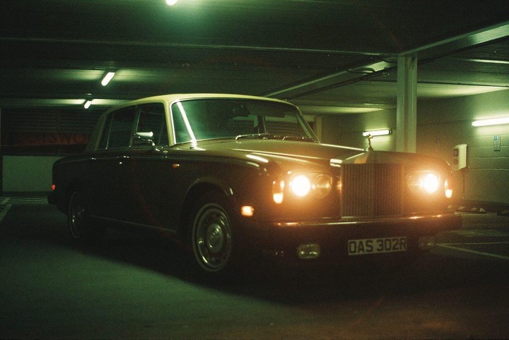 A classic car with its headlights on is parked in an underground garage.