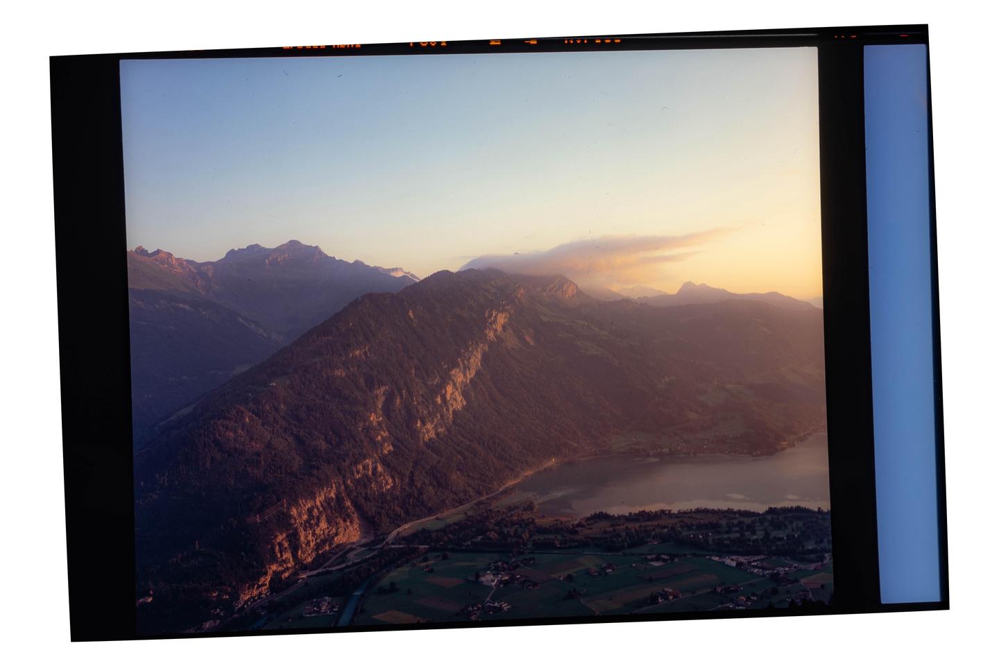 A panoramic landscape shows mountains, a lake, and a small village under a sunset sky.