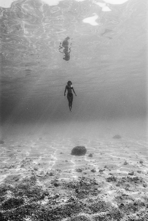 A woman in a bikini floats underwater above a sandy and rocky seabed.