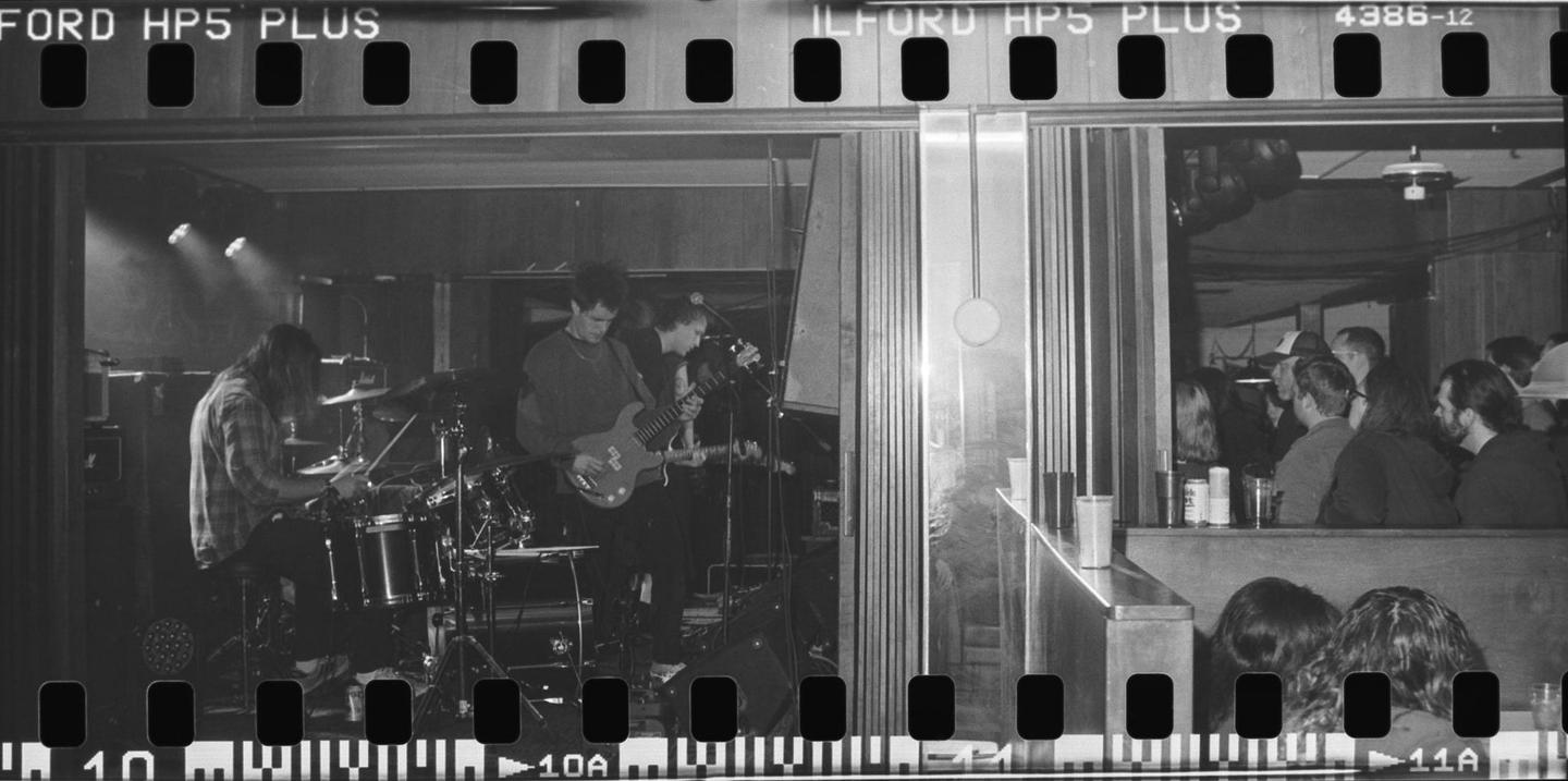 A band performs on stage while people watch from a bar area.