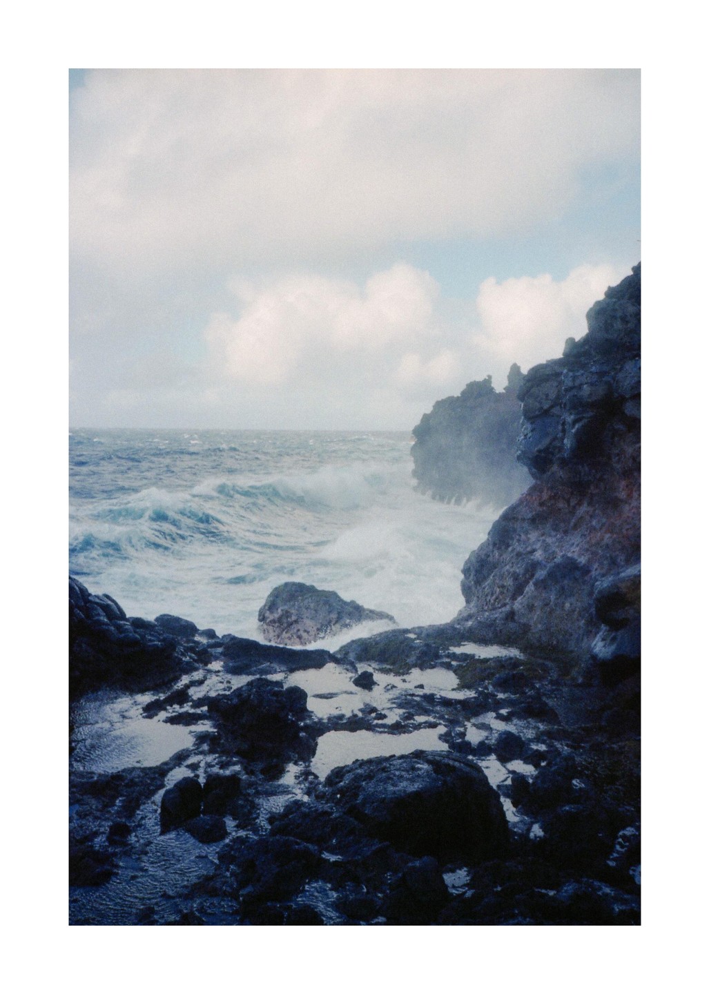 Waves crash against a rocky coastline under a cloudy sky.