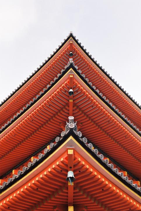 A low-angle view shows the corner of a multi-tiered pagoda roof with orange eaves and a small bell hanging from one of the corners.