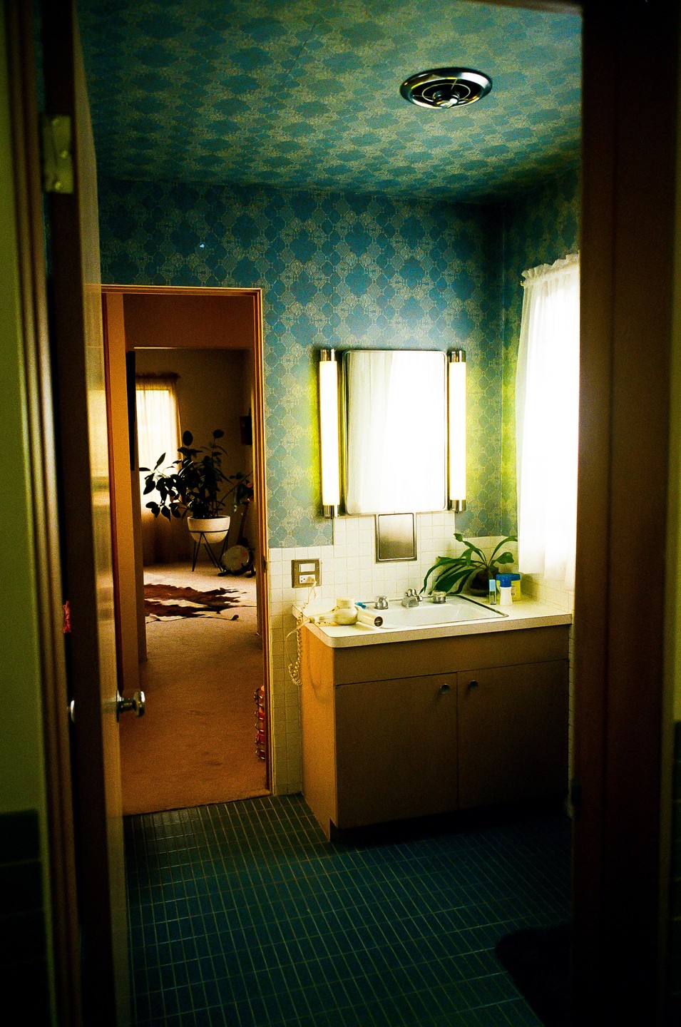 A bathroom with blue patterned wallpaper and tiled floor is visible through an open doorway, with another room visible beyond.