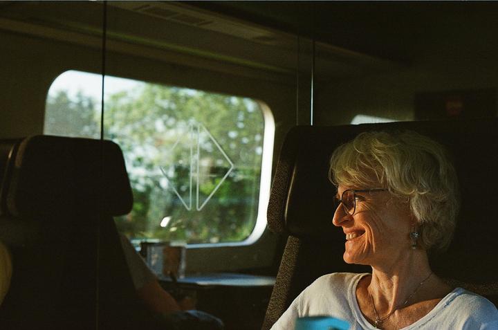A woman with glasses smiles while sitting in a train next to a window.
