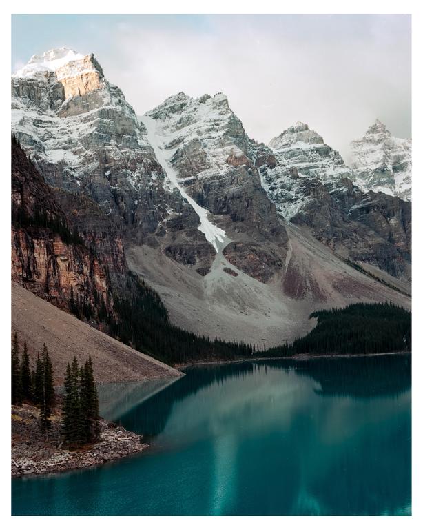 A turquoise lake reflects snow-capped mountains under a cloudy sky.