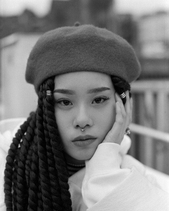 A woman with braided hair and a beret rests her chin on her hand.