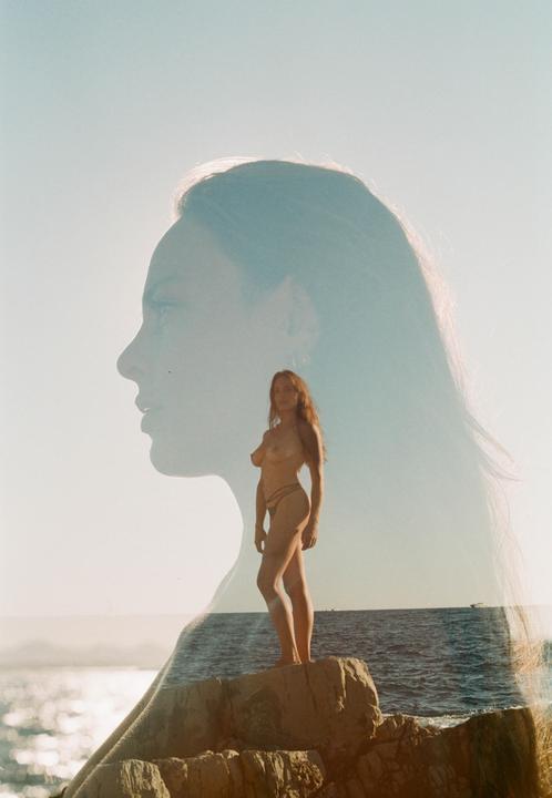 A double exposure shows a woman's profile superimposed over a woman standing on a rock by the sea.