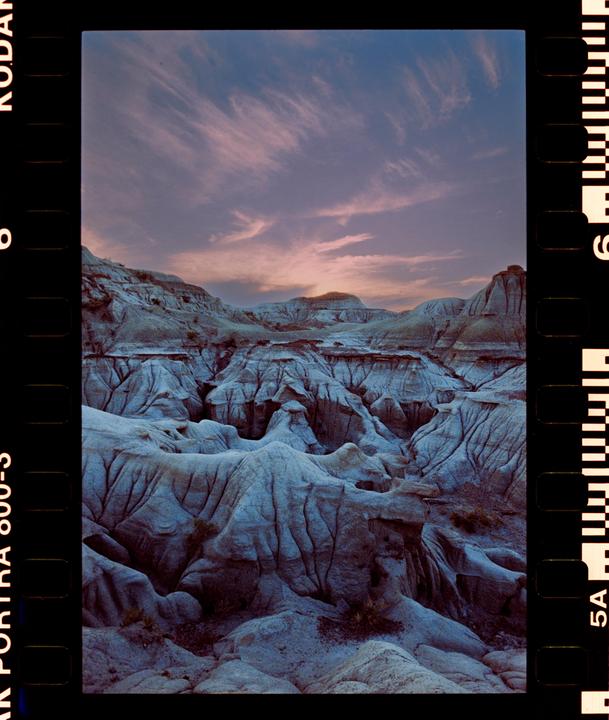 A vast landscape of eroded badlands is visible under a sky with wispy clouds at dusk.