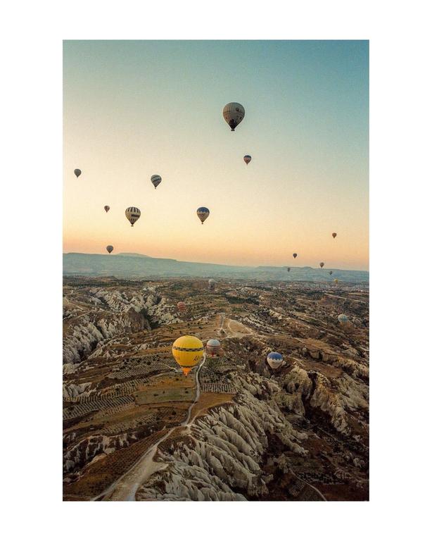 Hot air balloons float above a rugged, arid landscape with valleys and hills under a clear sky.