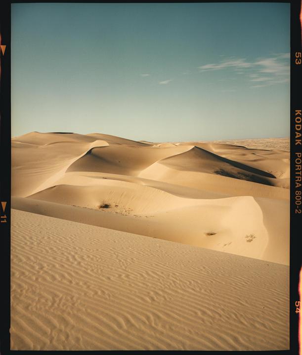 A vast desert landscape features numerous sand dunes under a clear sky.