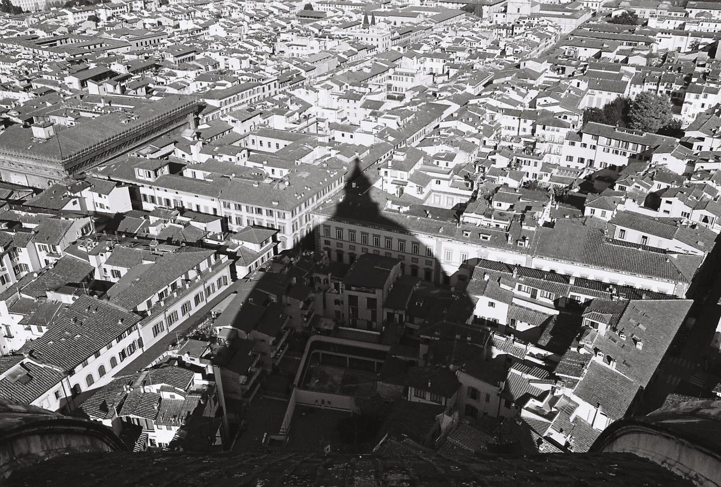 An aerial view shows a city with many buildings and a large shadow cast over them.