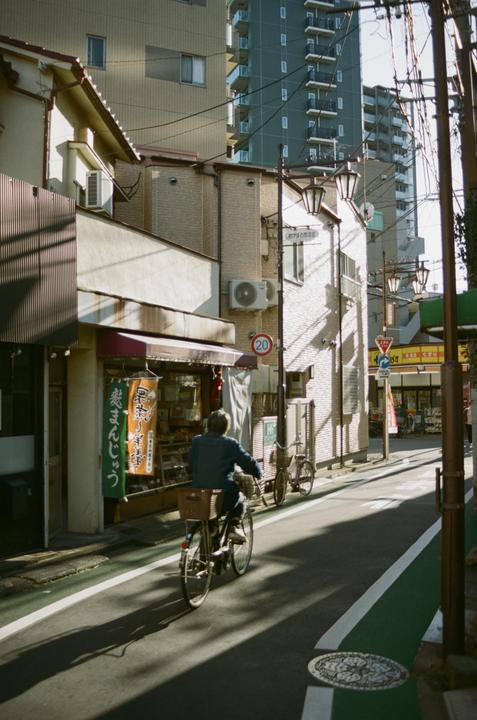A man rides a bicycle down a narrow street lined with buildings and power lines.