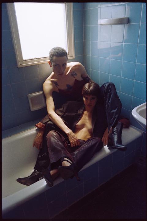 A couple is sitting in a bathtub in a bathroom with blue tiled walls.
