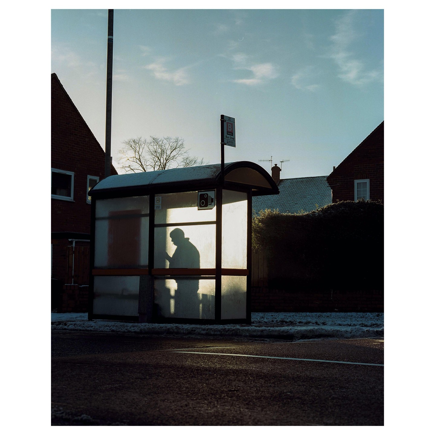 A man stands silhouetted in a bus stop shelter on a street.