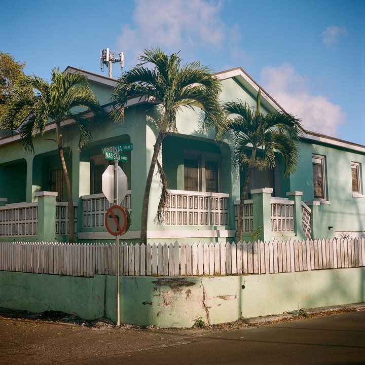 A mint green house with a white picket fence and palm trees stands at the corner of Virginia Street and Nassau Street.