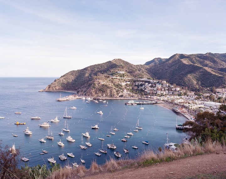 Many boats are moored in a harbor next to a town built into a hillside.