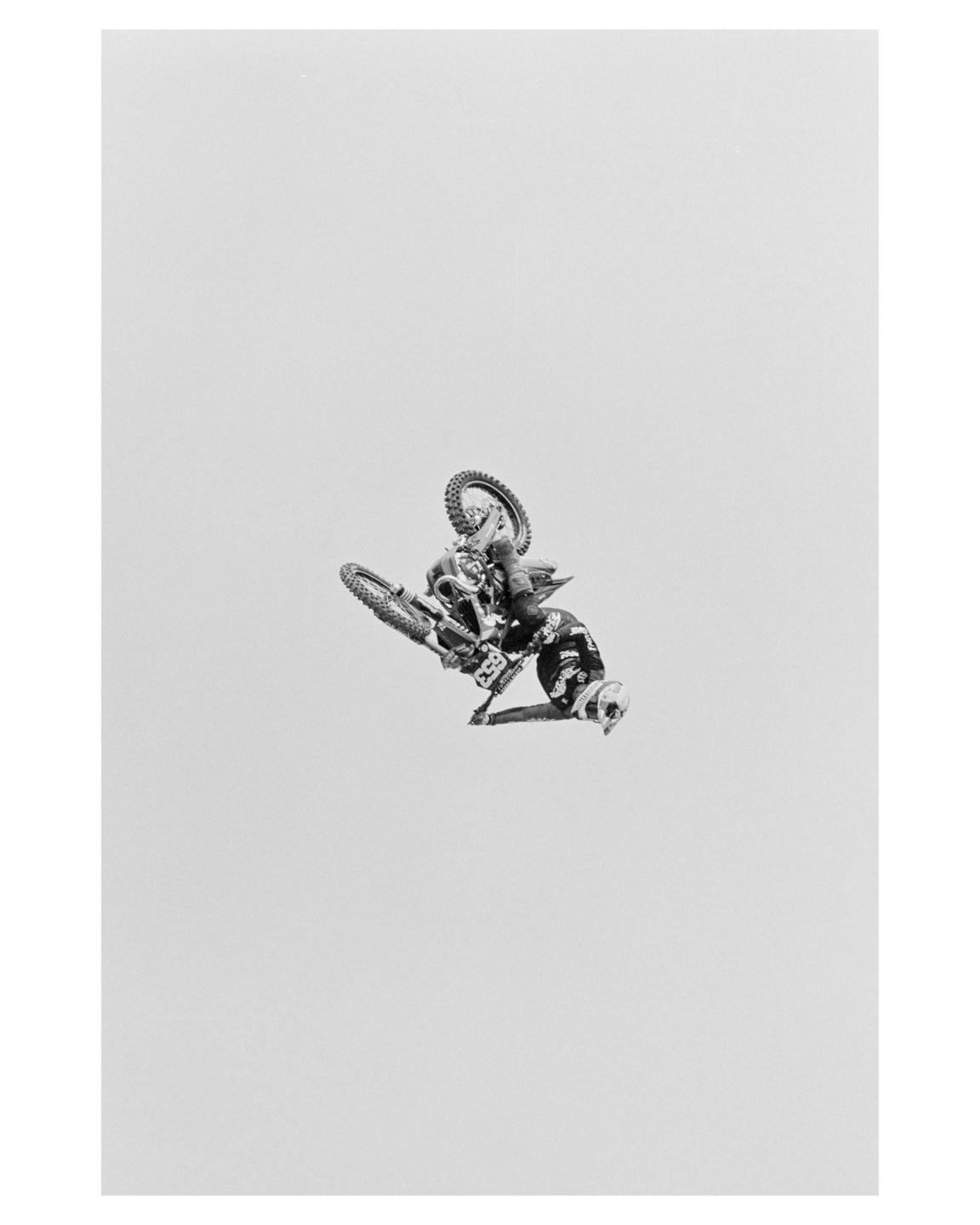 A motocross rider and their motorcycle are captured mid-air against a plain background.